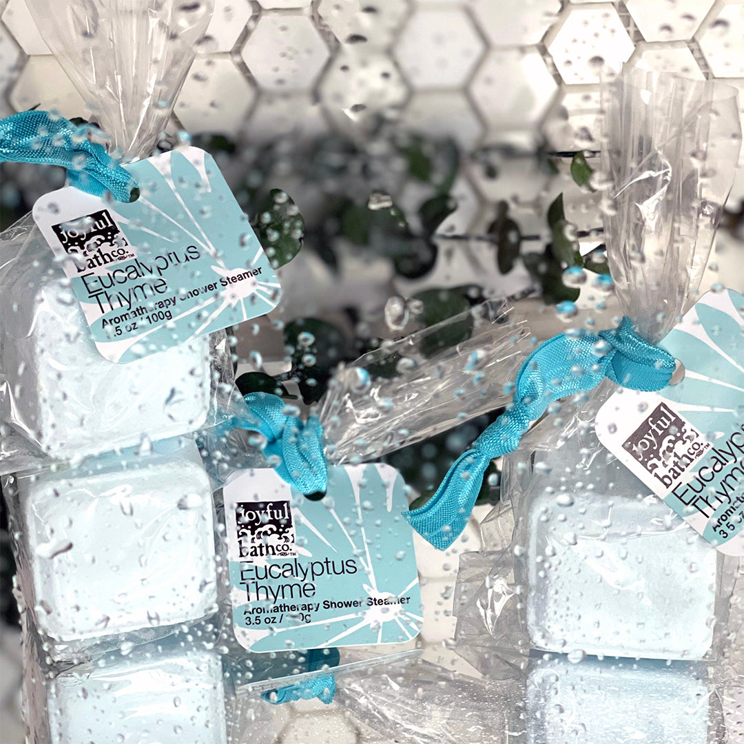 Three Eucalyptus Thyme Shower Steamers surrounded by drops of water and leaves behind them