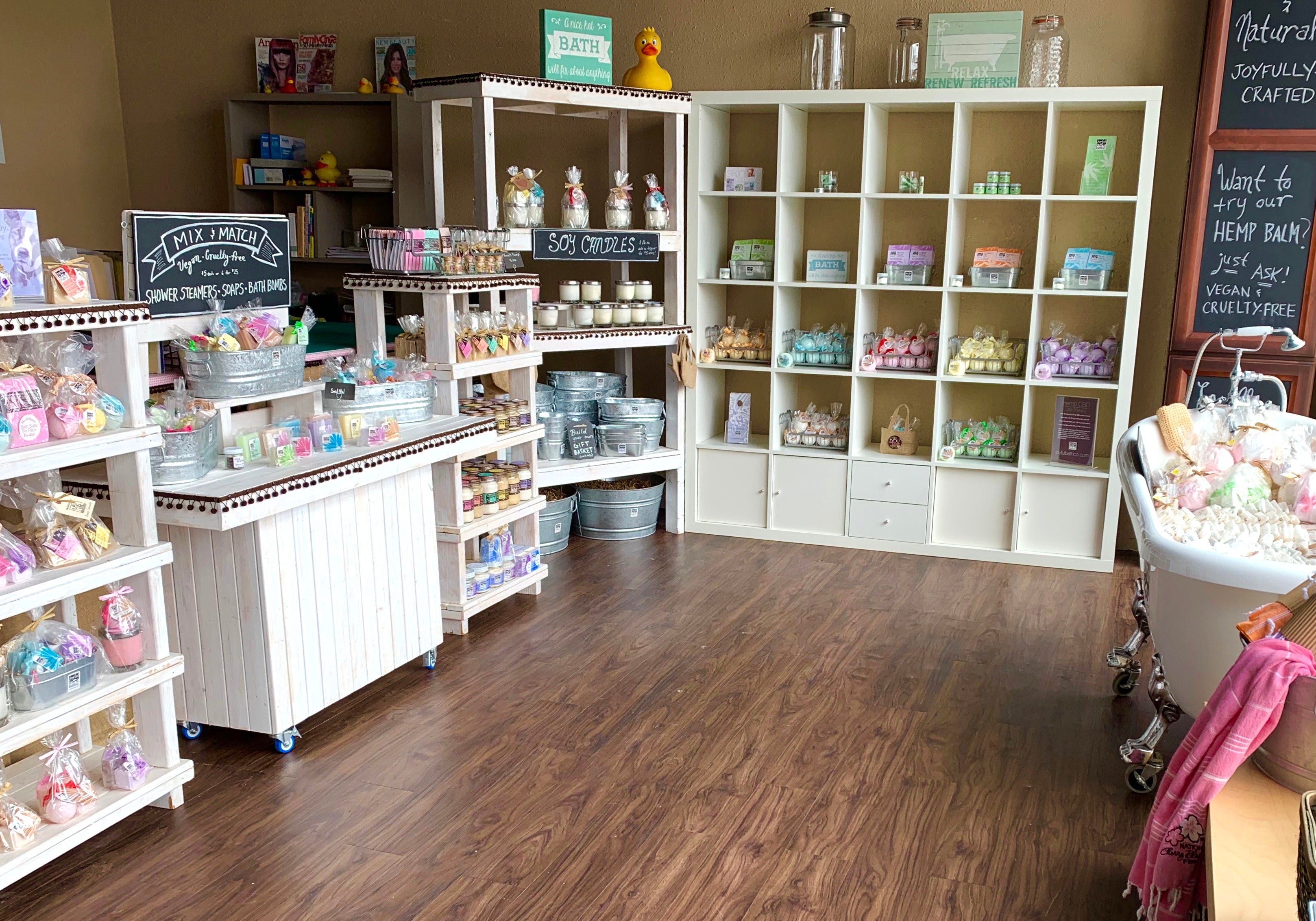 A boutique store with white shelves and products on the shelves. Brown floors and beige walls.