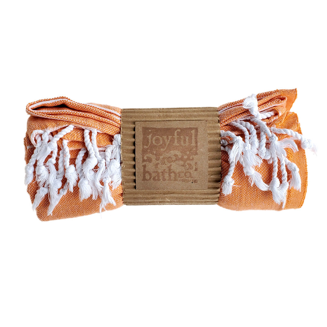 a rolled up orange towel with tassels in a kraft paper sleeve with a logo stamped over it