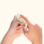 A hand scooping out hemp balm on a light yellow background