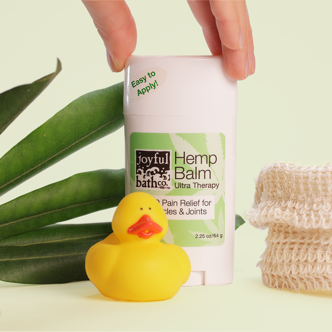 Hemp Balm with a rubber duckie in the foreground and leaves in the background with a natural fiber bag as a hold is reaching for the balm