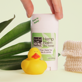 Hemp Balm with a rubber duckie in the foreground and leaves in the background with a natural fiber bag as a hold is reaching for the balm